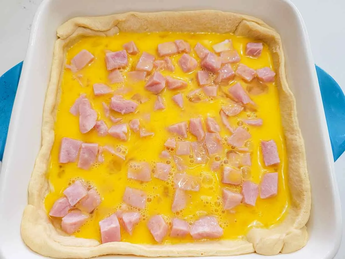 beaten egg and diced ham layered over crescent dough in a baking dish.
