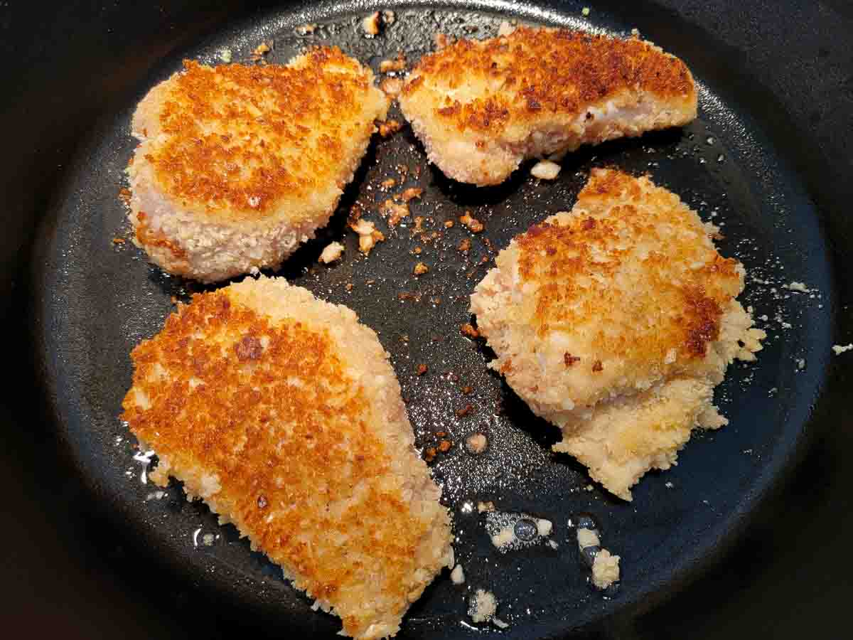 4 mac nut crusted chicken pieces cooking in a skillet.