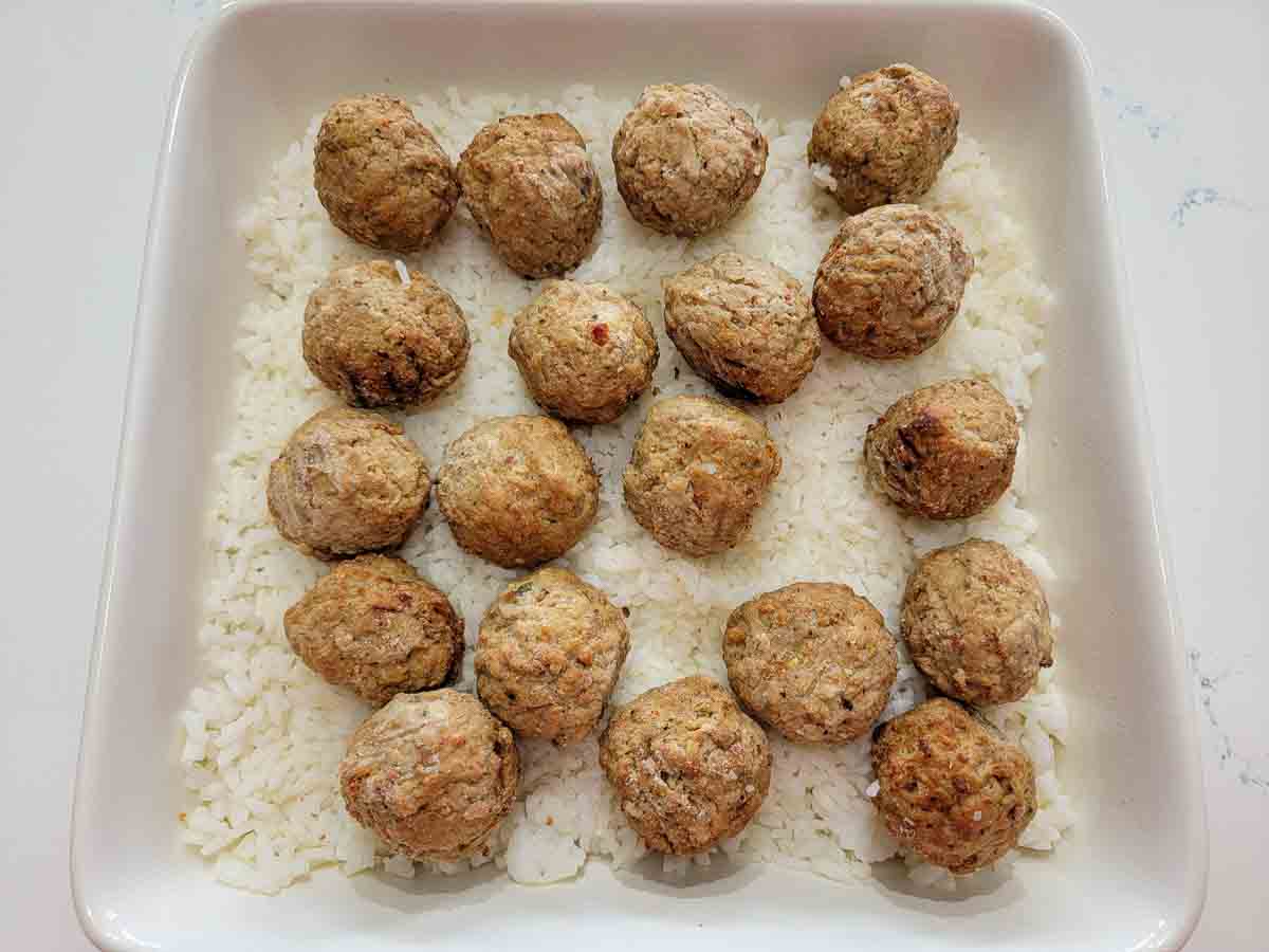 beef meatballs and cooked white rice in a square baking dish.
