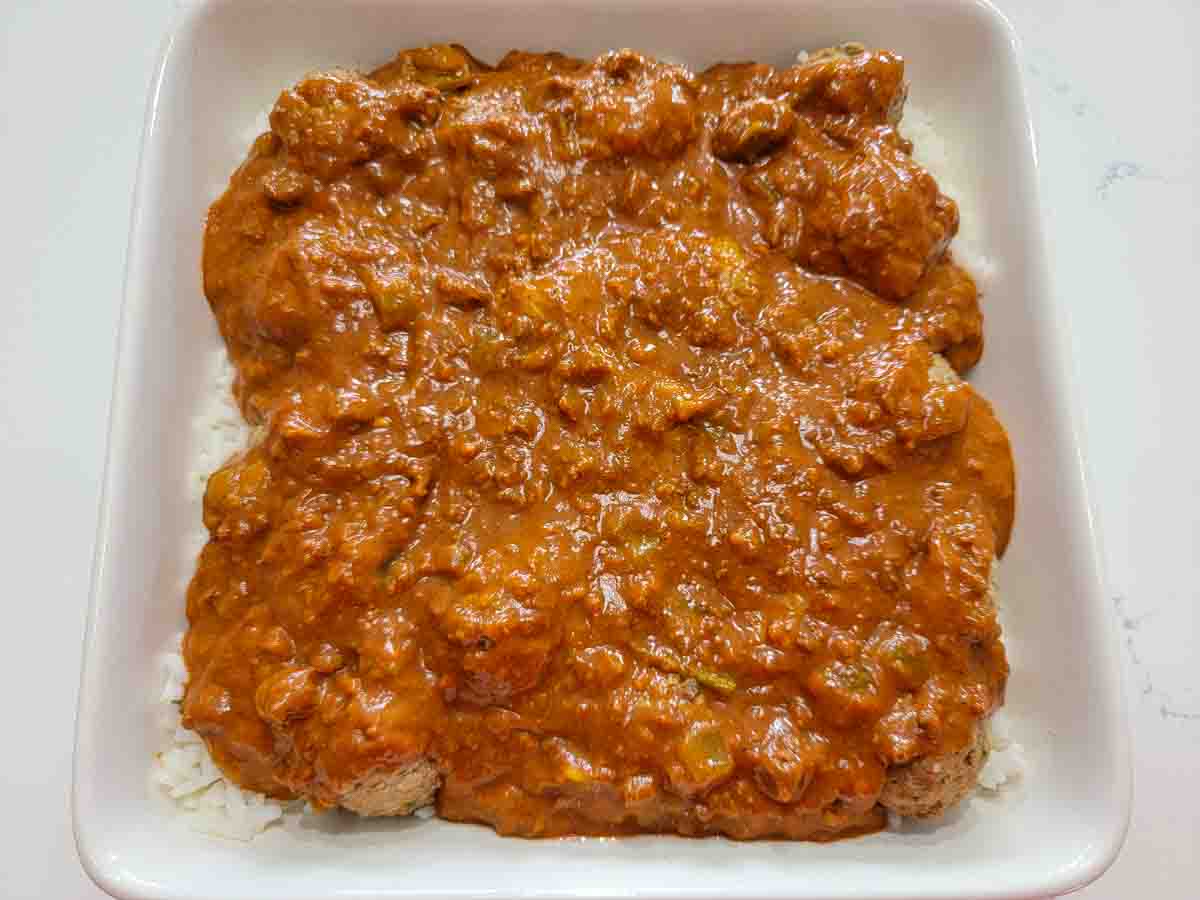 red sauce, beef meatballs and cooked white rice in a square baking dish.