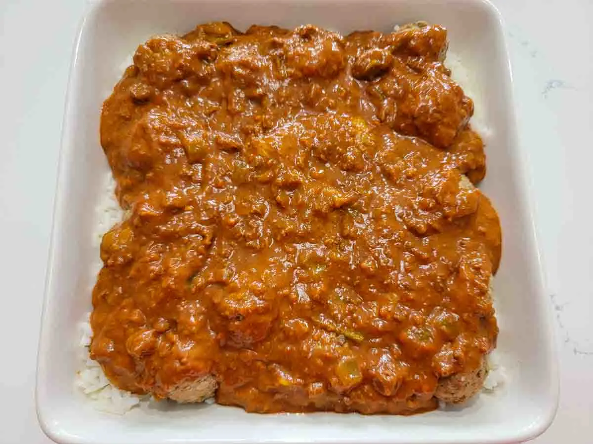 red sauce, beef meatballs and cooked white rice in a square baking dish.