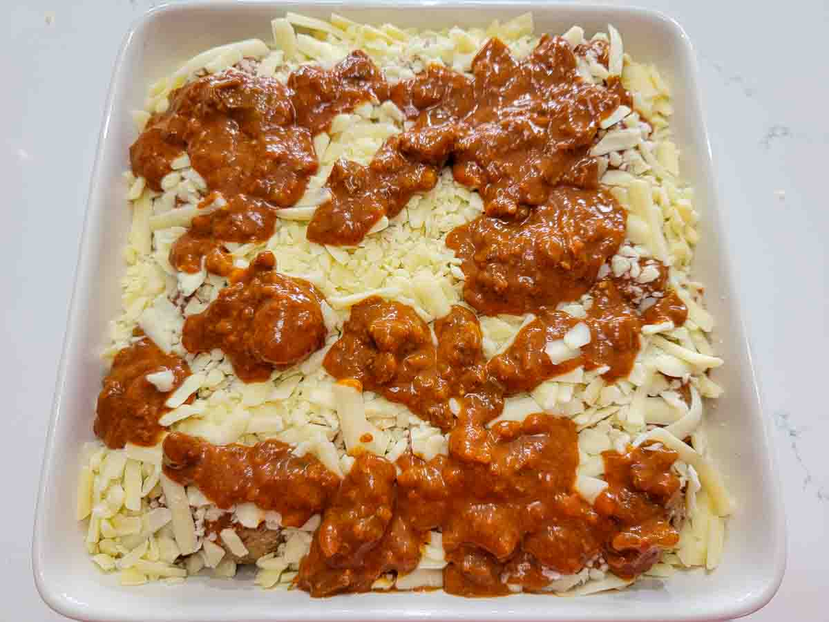 cheese, red sauce, beef meatballs and cooked white rice in a square baking dish.