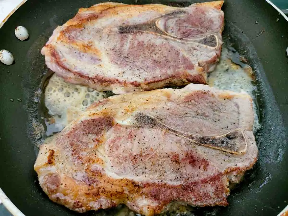 2 pork steaks frying in a pan.
