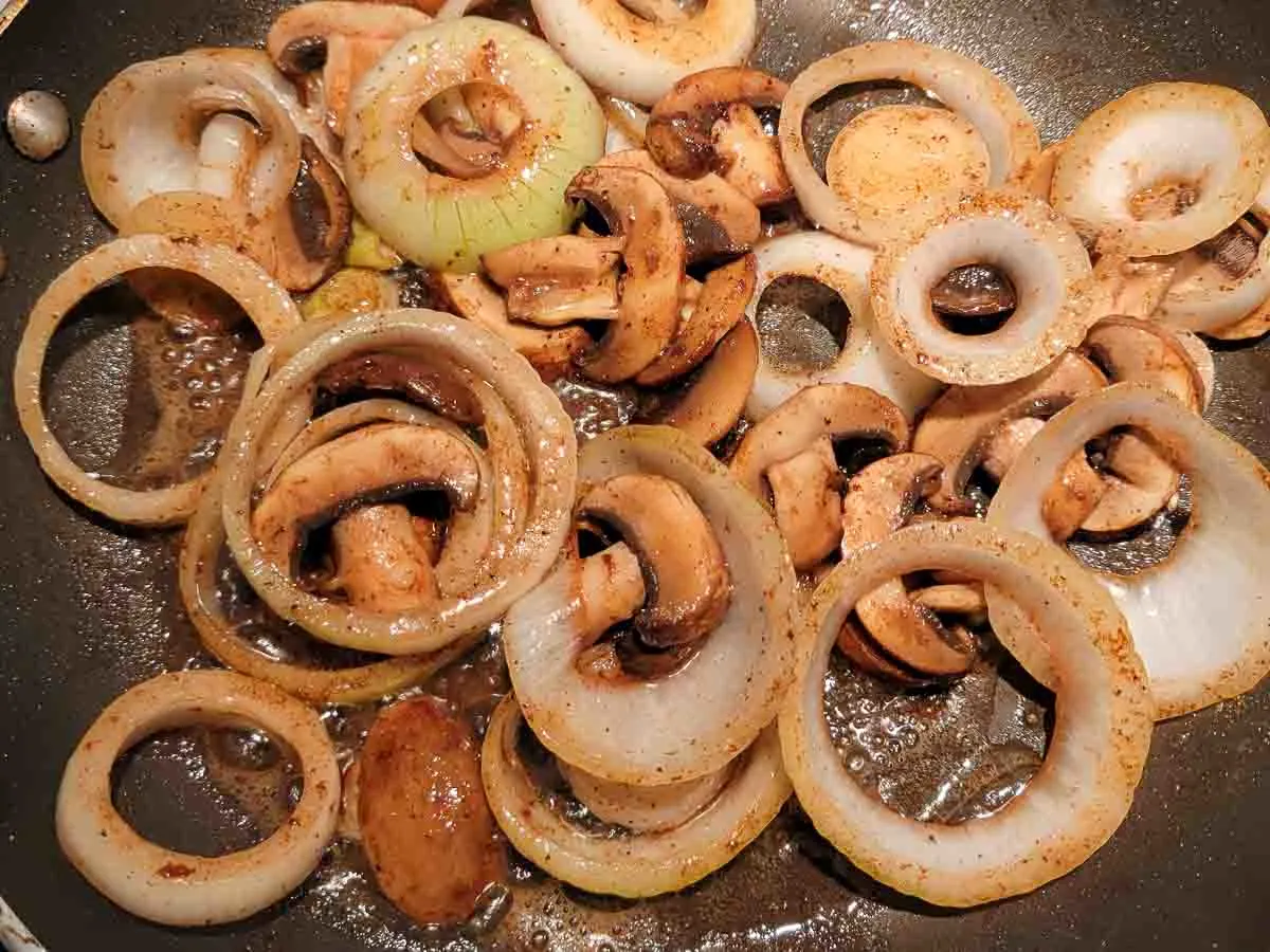 onion slices and mushroom slices cooking in a pan.