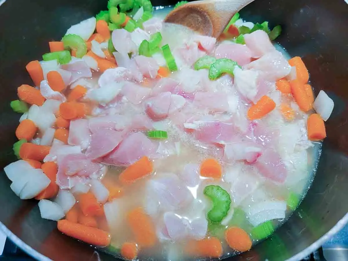 chicken broth, diced chicken, celery, onions, and carrots cooking in a pot.