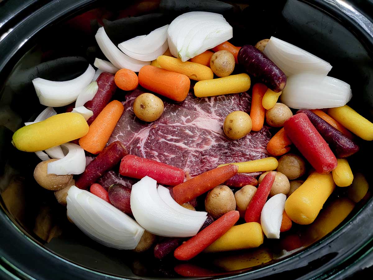 beef roast, onions, potatoes, and carrots in a crockpot.