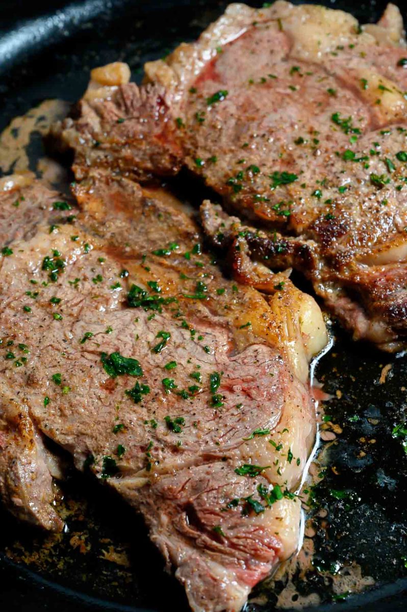 Cast Iron Skillet Ribeye Steaks cooking in a frying pan.