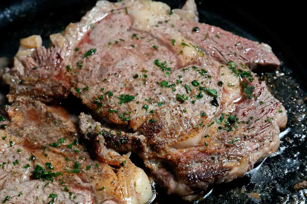 Cast Iron Skillet Ribeye Steaks cooking in a frying pan.