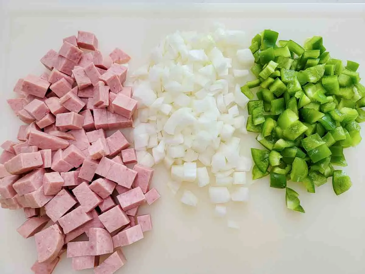 diced spam, onions, and green peppers on a cutting board.