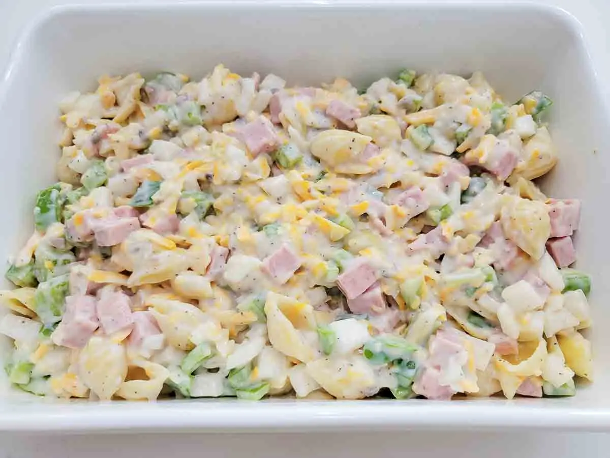 cooked pasta, soup, cheese, milk, onion, green pepper, and black pepper in a casserole dish.