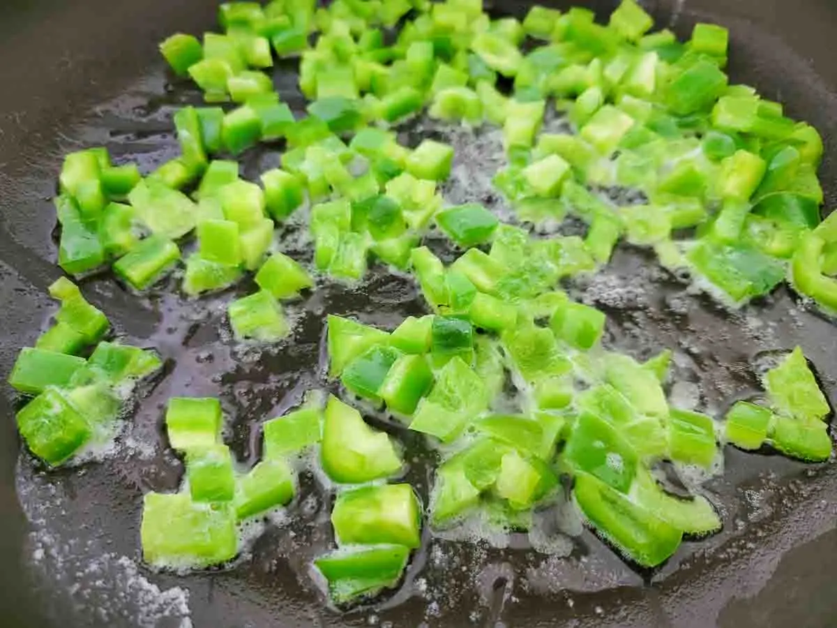 diced green peppers cooking in a skillet.