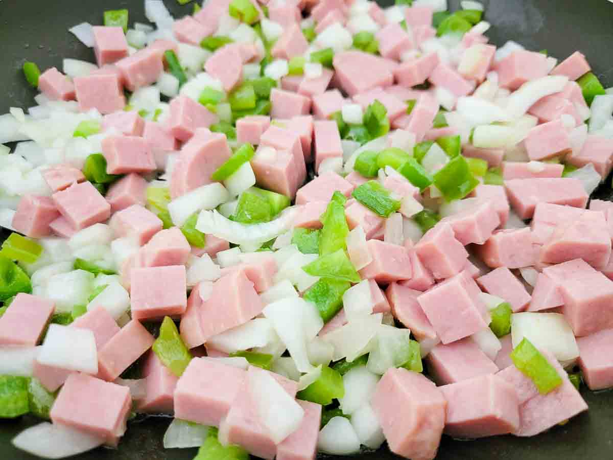 diced spam, diced onions, and diced green peppers cooking in a skillet.