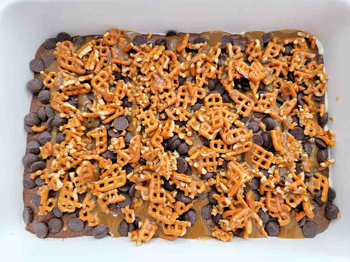 cake batter spread into a 9x13 cake pan and topped with crushed buttery pretzels, chocolate chips, and caramel sauce.