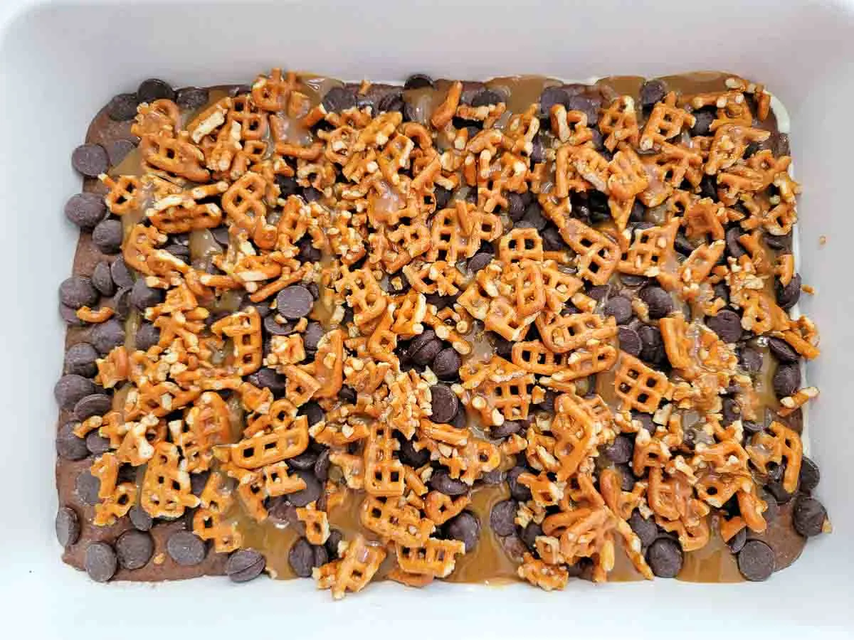 cake batter spread into a 9x13 cake pan and topped with crushed buttery pretzels, chocolate chips, and caramel sauce.