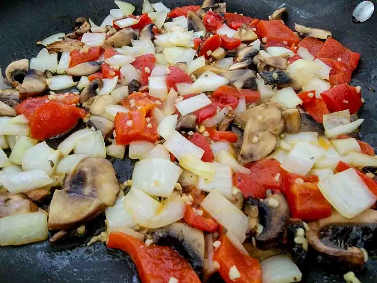 butter, minced garlic, onions, mushrooms, and roasted red peppers cooking in a skillet.