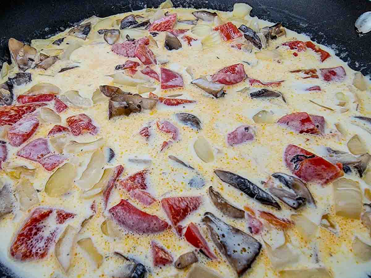 heavy cream, chicken broth, butter, minced garlic, onions, mushrooms, and roasted red peppers cooking in a skillet.