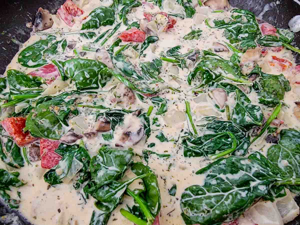 Italian seasoning, parsley, spinach, shredded parmesan cheese, heavy cream, chicken broth, butter, minced garlic, onions, mushrooms, and roasted red peppers cooking in a skillet.