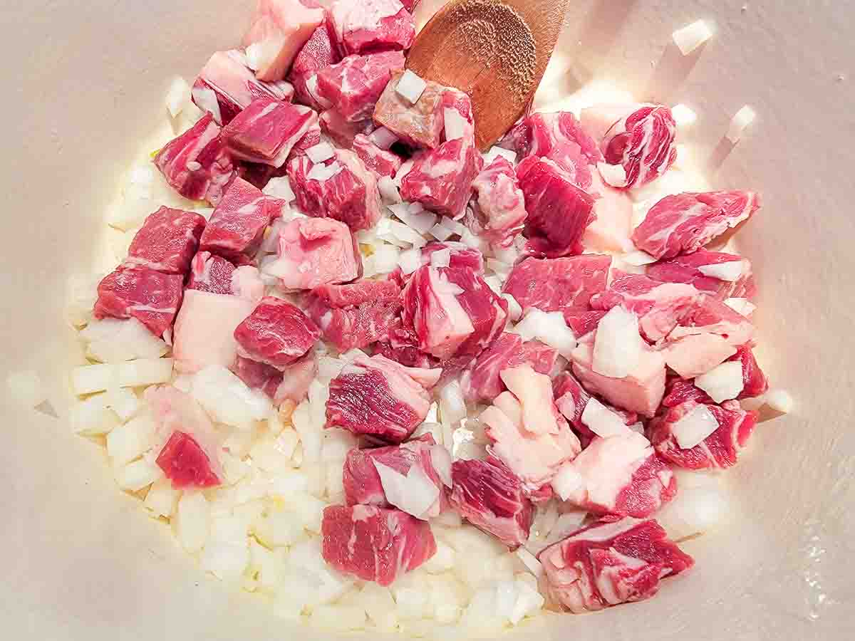 ribeye steak and diced onions cooking in a dutch oven.