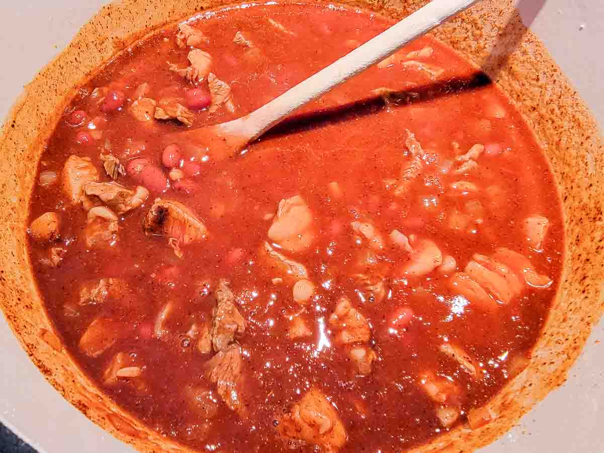 steak, onions, tomato sauce, chili beans, garlic salt, chili powder, beer, and cumin cooking in a pan.