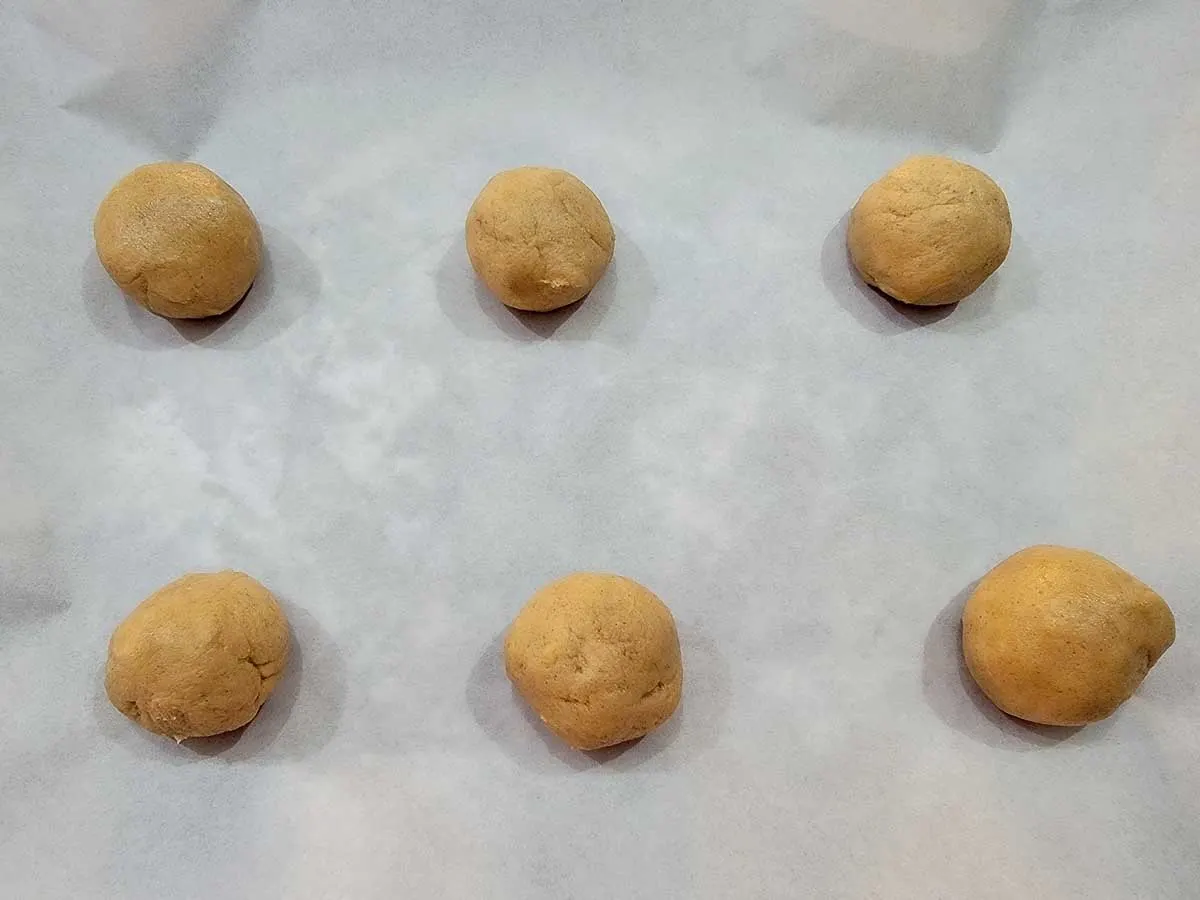 cookie dough balls on a parchment paper lined baking sheet.